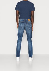 Maglietta blu scuro abbinata a jeans in denim azzurro. I jeans presentano un'etichetta in pelle sul retro e un design standard a cinque tasche.