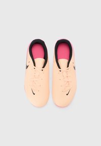 Oranžovo-meruňkové syntetické fotbalové boty s černým logem Nike, zaoblenou špičkou a růžovou gumovou podrážkou. Design na šněrování s černým interiérem.