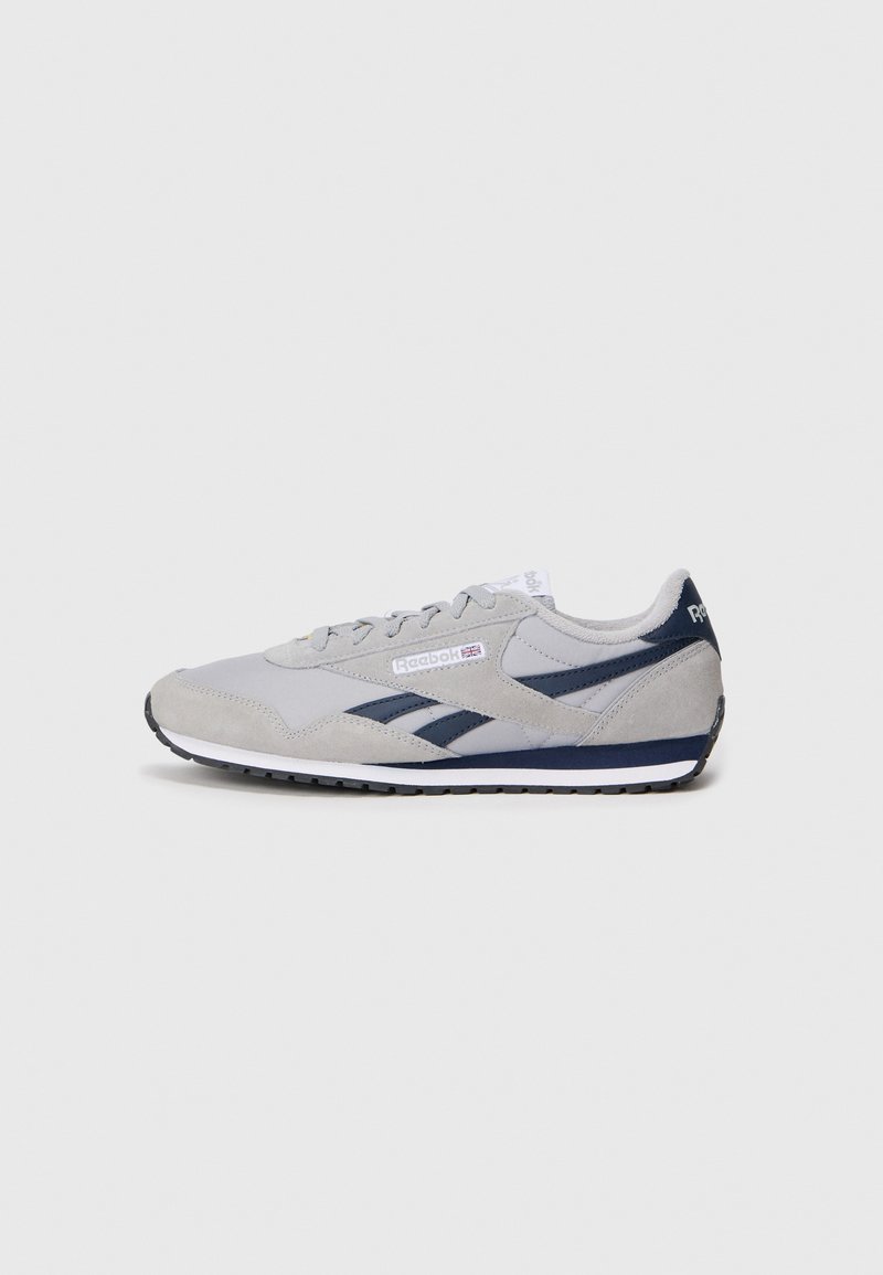 Sapatilha cinza em camurça e malha com detalhes em azul-marinho, biqueira redonda, atacadores planos e sola de borracha preta. Apresenta a marca Reebok na lateral.