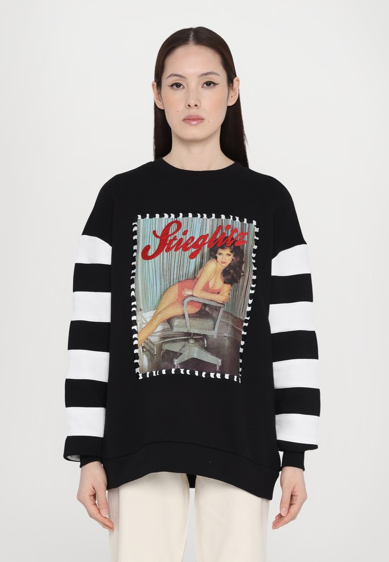 Black sweatshirt with striped white sleeves, featuring a graphic print of a seated figure against a striped backdrop, outlined with contrasting stitching.
