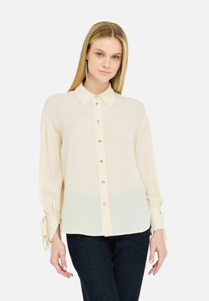 Blusa crema con colletto a punta, chiusura anteriore con bottoni e polsini arricciati. Realizzata in tessuto leggero con una texture liscia.