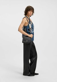 Top in seta con un motivo astratto blu e bianco, abbinato a pantaloni in pelle nera a gamba larga e una borsa nera strutturata.