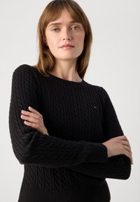 Černý svetr s pleteninou, který má žebrovaný výstřih a manžety, navržený s texturovaným vzorem a malým logem.