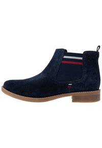 Botas de tobillo de gamuza azul marino con paneles laterales elásticos que presentan rayas rojas y blancas, suela de goma marrón y una lengüeta en el talón.
