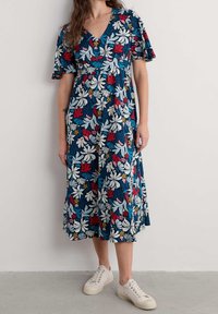 Robe midi florale bleu marine à manches courtes volantées, ornée de fleurs blanches, rouges et jaunes, associée à des baskets blanches.
