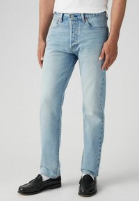 Vaqueros de mezclilla azul claro con un corte recto, diseño clásico de cinco bolsillos y cierre de botón, llevados con mocasines negros.