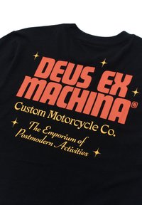 Black t-shirt featuring bold red text "DEUS EX MACHINA" and gold accents. Text includes "Custom Motorcycle Co." and "The Emporium of Postmodern Activities."