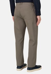Pantalon beige à coupe droite, avec une texture lisse, deux poches arrière et une petite étiquette de marque sur la ceinture.