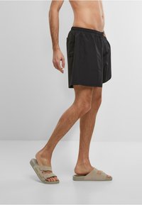 Sorte svømshorts med elastisk talje og sidelommer; parret med beige sandaler med dobbeltstrop og logo.