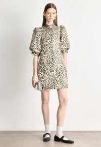Sukienka w panterkę z krótkimi bufkami, kołnierzem, zaszewką w talii i dopasowanym krojem; zestawiona z czarnymi butami Mary Jane i białymi skarpetkami.