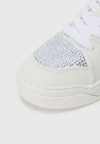 Hvit sneakers med en glatt skinnoverdel og et panel dekorert med sølv rhinestones, strukturert gummisåle og hvite lisser.