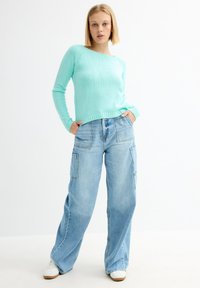 Suéter de punto azul claro con mangas largas, combinado con pantalones cargo de denim de lavado claro, holgados y con bolsillos laterales.