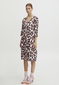 Robe à imprimé léopard en tissu doux, décolleté en V, manches trois-quarts, longueur jusqu'au genou, associée à des talons et des chaussettes aux accents rose clair et orange.