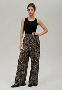 Svart tanktopp kombinert med vide bukser med et brunt og beige leopardmønster, designet med høy midje og myk stoff.