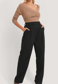 Ribbad brun långärmad topp med asymmetrisk halsringning, kombinerad med högmidjade svarta plisserade byxor med sidofickor.