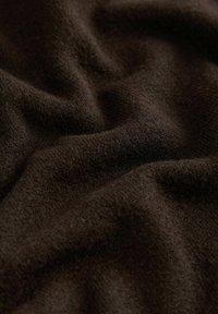 Pehmeä, tumma ruskea villa-aine, jossa on näkyvä rakenne ja lempeät taitteet, jotka luovat hieman aaltoilevan pinnan.