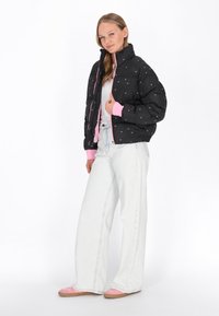 Sort pufferjakke med lyserøde detaljer, quiltet tekstur og grafisk tryk. Parret med lyseblå bredbukser og lyserøde sko.