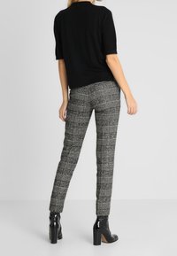 Suéter negro de manga corta combinado con pantalones ajustados de cuadros grises y botas negras de charol con tacón cuadrado, mostrando una silueta elegante.