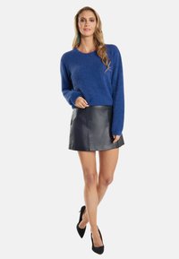 Kék, bolyhos pulóver hosszú ujjal, amelyet egy fekete bőr miniszoknyával párosítottak. Az outfitet fekete magassarkú cipők egészítik ki.