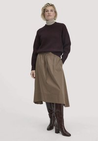 Brauner gerippter Pullover, beiger Rollkragenpullover, bra-skirt mit elastischem Bund, knielange dunkelbraune Stiefel mit Absatz, stehend vor einem hellen Hintergrund.