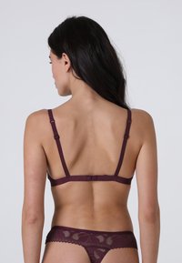 Reggiseno in pizzo bordeaux con spalline regolabili, caratterizzato da un motivo floreale e chiusura a gancio sul retro. Texture liscia con un design delicato.