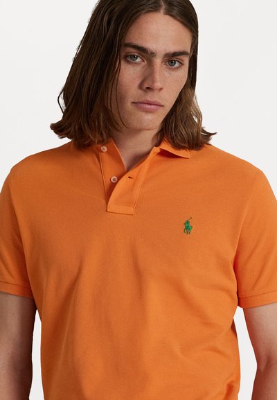 Oranje polo shirt van gestructureerde katoen, met een drieknopenlijst en een groen logo op de linkerkant van de borst.