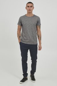 Šedé melírované tričko s kulatým výstřihem, doplněné námořnickými slim-fit kalhotami a černými teniskami s bílými podrážkami. Pohodlný outfit.