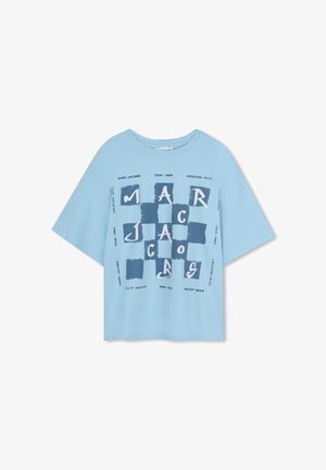T-shirt en coton bleu clair avec manches surdimensionnées, arborant une impression graphique en bleu foncé et un texte blanc indiquant l'année et le lieu.