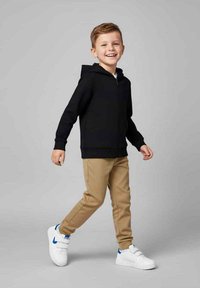 Czarna bluza z kapturem na zamek, beżowe spodnie i białe trampki z niebieskimi akcentami. Dziecko uśmiecha się i spaceruje na szarym tle.