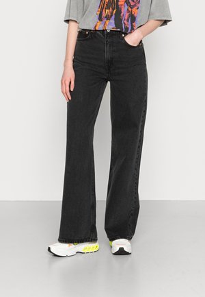 Jeans negros de cintura alta con diseño de pierna recta, con el clásico estilo de cinco bolsillos y un acabado texturizado sutil. Combinados con zapatillas blancas.