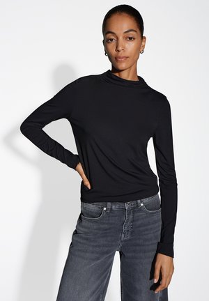 Zwarte langwerpige top met een hoge hals en zachte textuur, gecombineerd met donkergrijze jeans. Eenvoudig ontwerp, zonder patronen of versieringen.