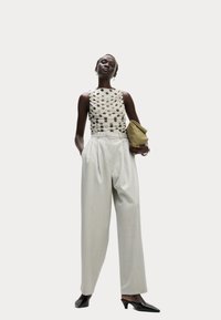 Top bianco senza maniche con pois neri, pantaloni grigi chiari a vita alta e una pochette verde oliva con texture. Tacchi neri a punta.