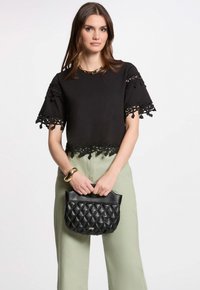 Sort cropped top med blondekant, grønne højhalset bukser og sort quiltet håndtaske. Guldarmbåndet fremhæver outfittet.