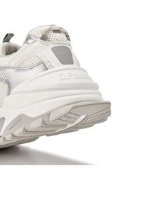 Zapatilla deportiva gruesa blanca con parte superior de malla texturizada, acentos plateados y una suela gruesa que presenta un patrón de relieve único para mayor agarre.