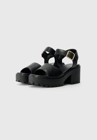 Schwarze Ledersandalen mit Plattform, zwei breiten vorderen Riemen und einem Knöchelriemen mit einer goldfarbenen Schnalle. Dicke, strukturierte Sohle für besseren Halt.