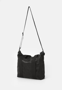 Svart totebag laget av teksturert stoff med doble robuste stropper, justerbar crossbody stropp og glidelås-lukking. Enkelt rektangulært design.