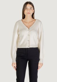 Cárdigan de punto marfil con escote en V, diseño corto, botones grandes, textura acanalada y mangas largas, combinado con pantalones negros.