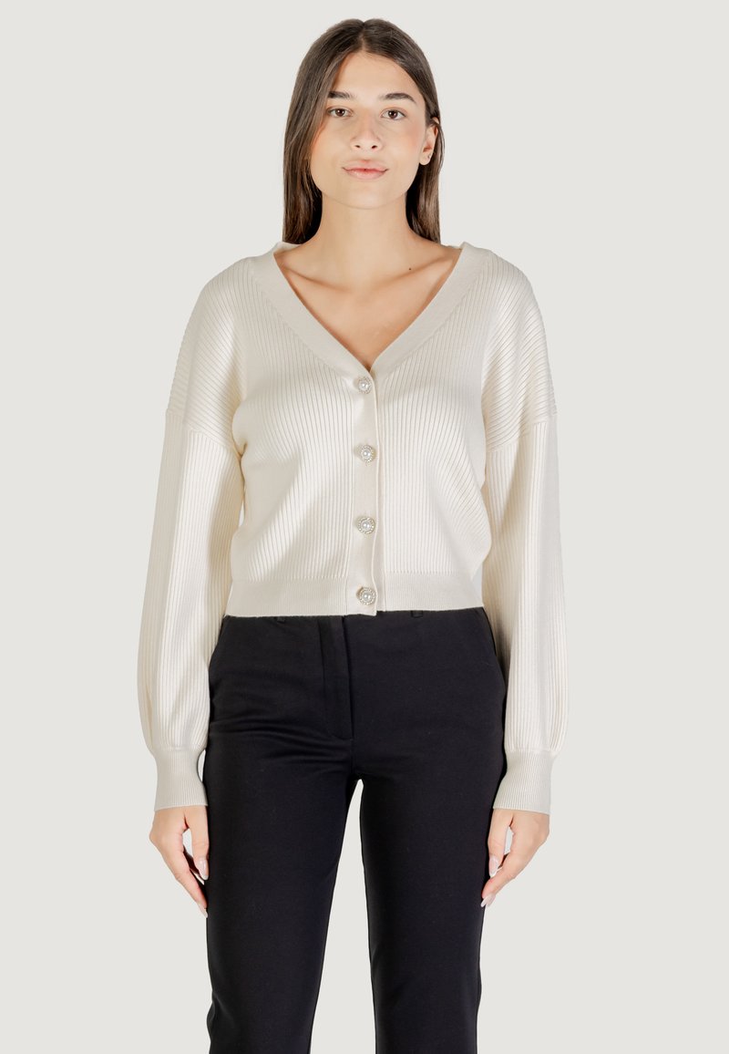 Cárdigan de punto marfil con escote en V, diseño corto, botones grandes, textura acanalada y mangas largas, combinado con pantalones negros.