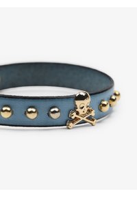 Bracciale in pelle di un blu chiaro con borchie dorate e un accento con teschio e ossa incrociate. Materiale texturizzato con bordi a contrasto.
