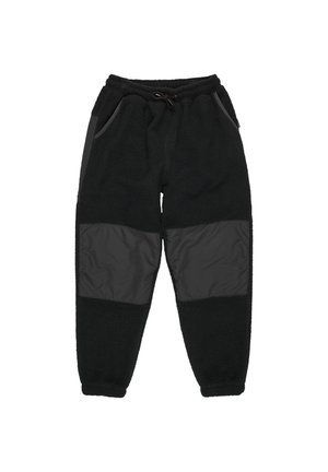 Boy wearing orange beanie, dark long-sleeve shirt with logo, black fleece pants, and brown New Balance sneakers, standing with hands in pockets.