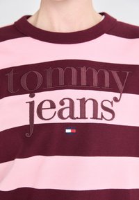 Sudadera de rayas granate y rosa con los textos bordados "tommy" y "jeans", con un pequeño logo tricolor debajo.