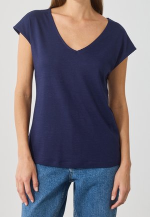 T-shirt bleu marine à col en V avec des manches courtes, fabriqué dans un matériau doux. Design simple et épuré avec une coupe décontractée. Porté avec un jean bleu clair.