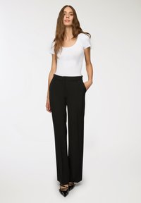 Pantaloni neri a gamba larga con una texture liscia, caratterizzati da una vestibilità tailored e tasche laterali. Abbinati a un top bianco aderente con scollatura a barca.