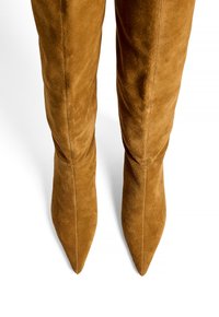 Bottes en suède couleur camel, au-dessus du genou, avec des pointes effilées et un design ajusté, présentant des coutures visibles le long des seams.
