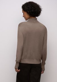 Pull à col roulé beige avec des manches longues, bords côtelés et ourlet, fabriqué dans un matériau doux, présentant une texture subtile et une coupe décontractée.