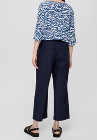 Top blu seguito a maniche corte con vestibilità ampia, abbinato a pantaloni croppati blu scuro e sandali neri, dotato di vita elastica e due tasche posteriori.