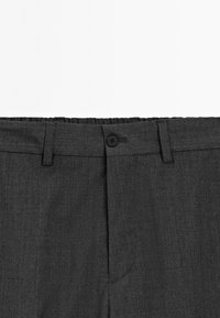 Pantaloni grigi scuri con fronte piatto, vita elastica e chiusura a un bottone, caratterizzati da una leggera texture e senza motivi visibili.