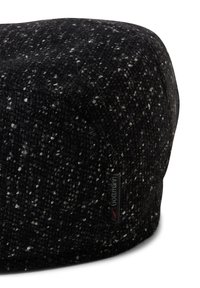 Czarnobiały ottoman o zaokrąglonym kształcie, wykonany z tkaniny plecionej, z małą, markową metką po boku.