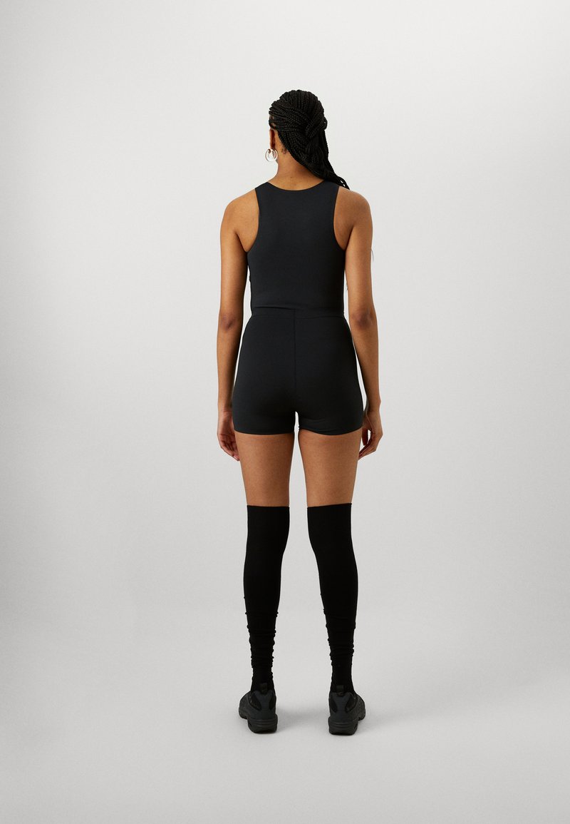 Bodysuit negro sin mangas con pantalones cortos ajustados, combinado con calcetines negros hasta la rodilla y calzado oscuro. Material suave y elástico con un diseño minimalista.