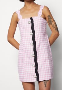 Rosa och vit rutig klänning med volangärmar, svart centralt kantband och dekorativa knappar med pärlaccent.